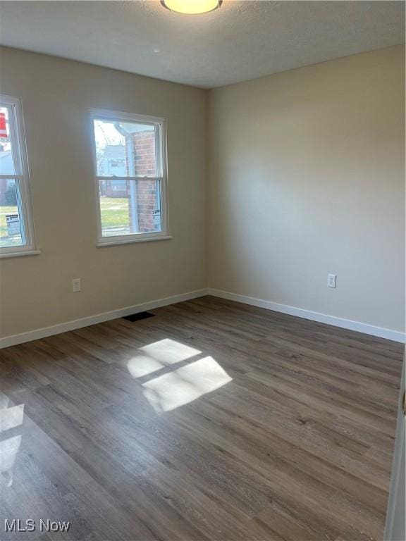 spare room with dark wood finished floors, plenty of natural light, and baseboards