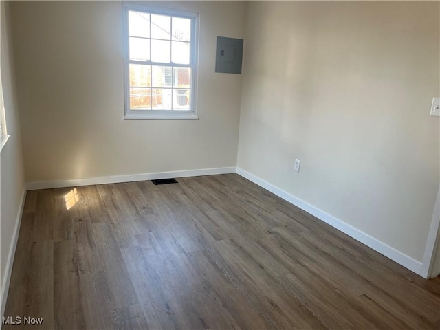 empty room with electric panel, visible vents, baseboards, and dark wood finished floors