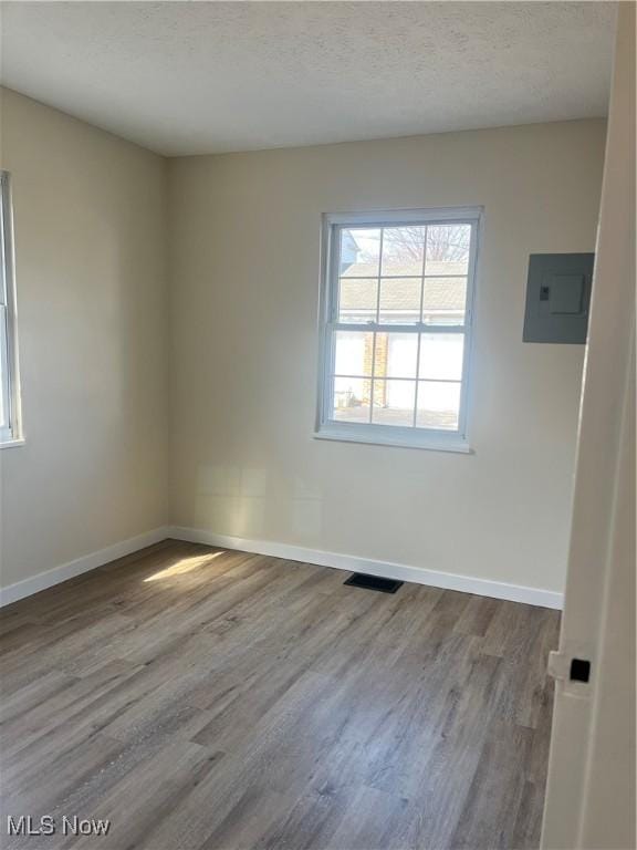 unfurnished room with visible vents, electric panel, a textured ceiling, wood finished floors, and baseboards