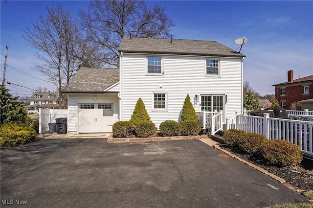 rear view of property featuring driveway, a garage, and fence