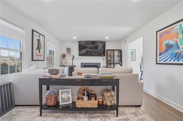 living area with radiator, baseboards, recessed lighting, a fireplace, and wood finished floors