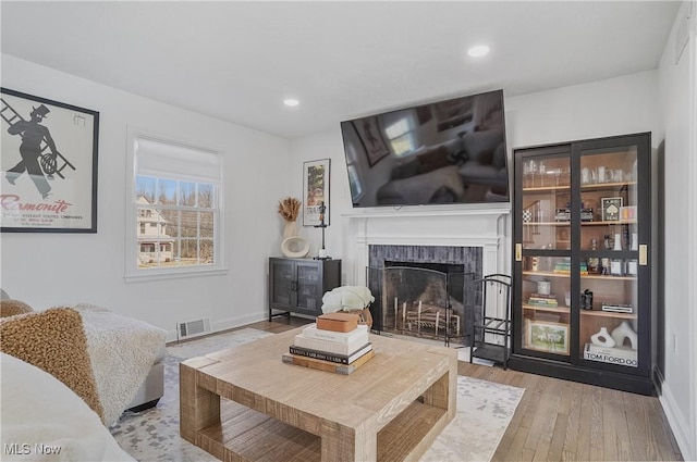 living room featuring visible vents, baseboards, recessed lighting, wood-type flooring, and a brick fireplace