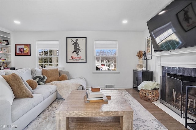 living room with recessed lighting, wood finished floors, visible vents, and a high end fireplace