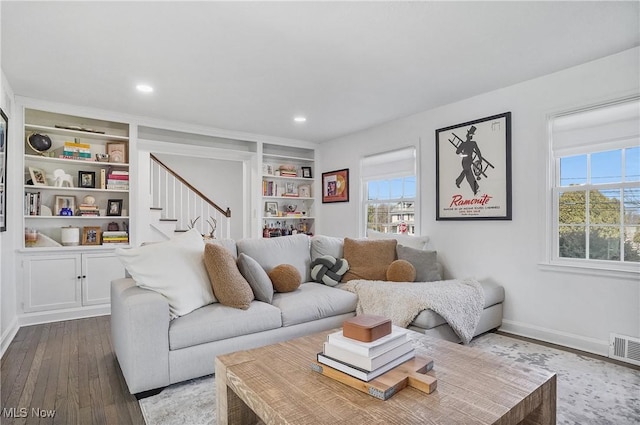 living room featuring visible vents, built in shelves, dark wood finished floors, stairway, and baseboards