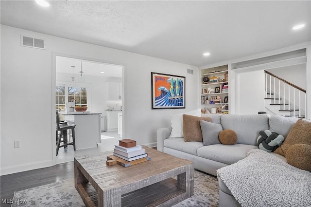 living room with visible vents, built in shelves, baseboards, recessed lighting, and wood finished floors