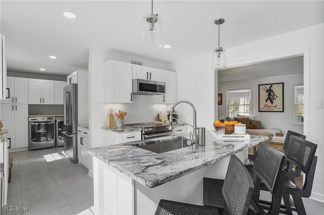 kitchen featuring stainless steel appliances, a breakfast bar area, white cabinets, decorative backsplash, and light stone countertops