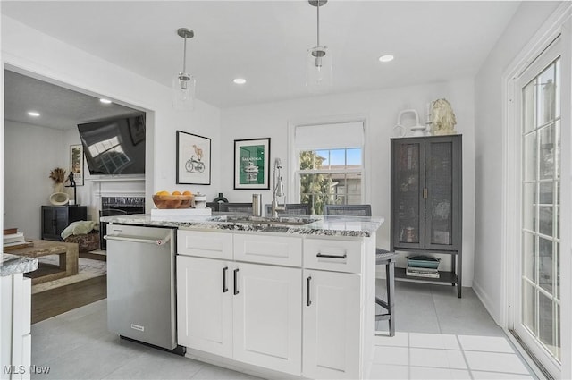 kitchen featuring light stone countertops, light tile patterned floors, hanging light fixtures, white cabinets, and a sink