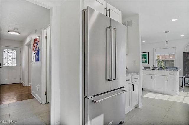 kitchen with high end refrigerator, a healthy amount of sunlight, and white cabinets