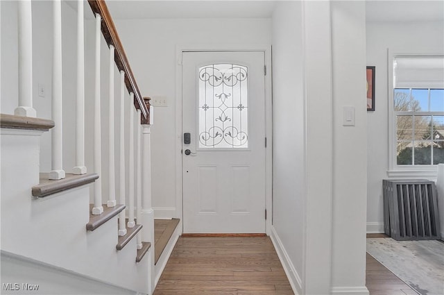 foyer with stairs, radiator, wood finished floors, and baseboards