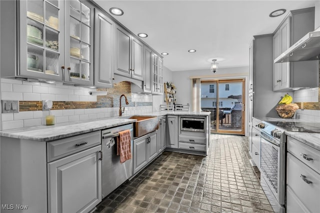 kitchen featuring stainless steel appliances, a peninsula, gray cabinets, and wall chimney range hood