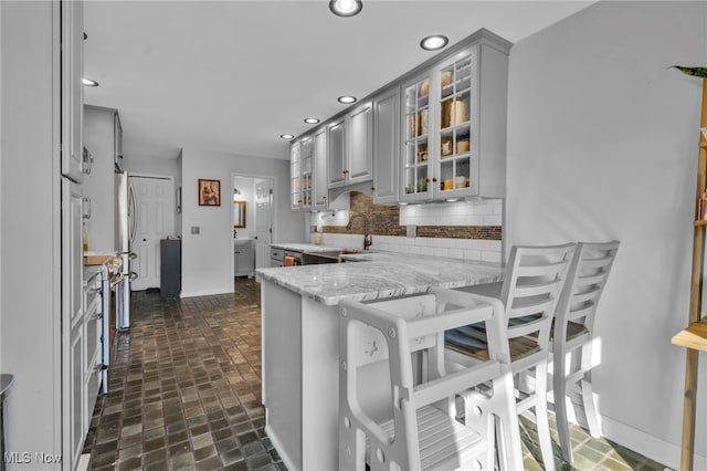 kitchen featuring a peninsula, recessed lighting, gray cabinets, a sink, and backsplash