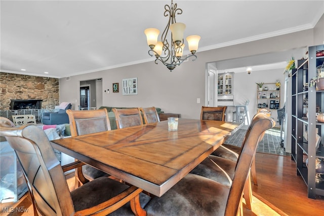 dining room featuring a notable chandelier, a stone fireplace, wood finished floors, and ornamental molding