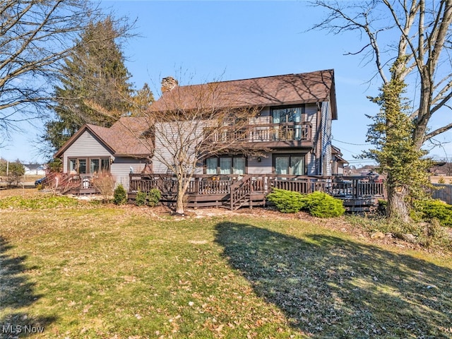 rear view of house with a deck, a lawn, a balcony, and a chimney