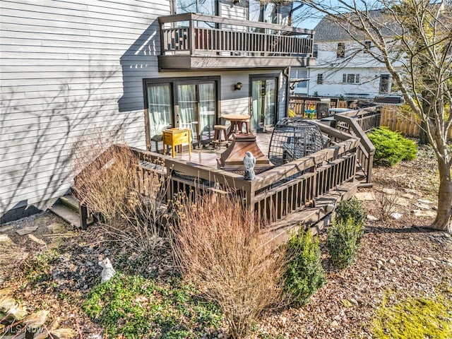 rear view of property with a balcony, a deck, and fence