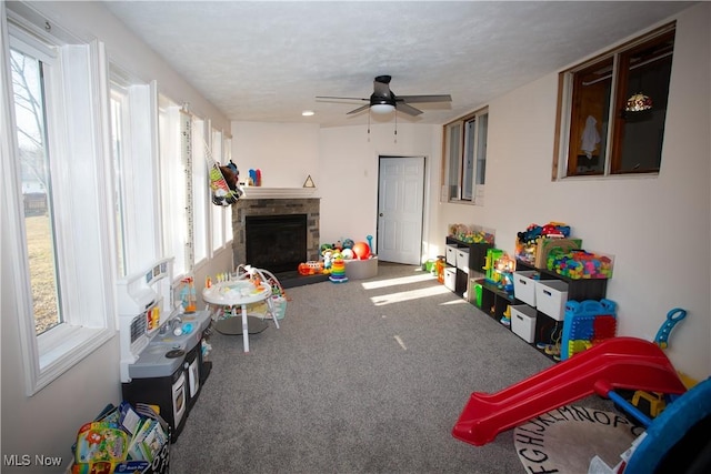 playroom with carpet flooring, a fireplace with raised hearth, a textured ceiling, and ceiling fan