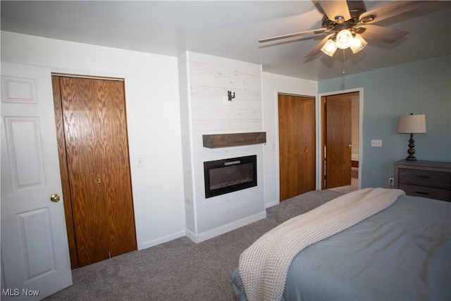 carpeted bedroom with ceiling fan, baseboards, multiple closets, and a glass covered fireplace