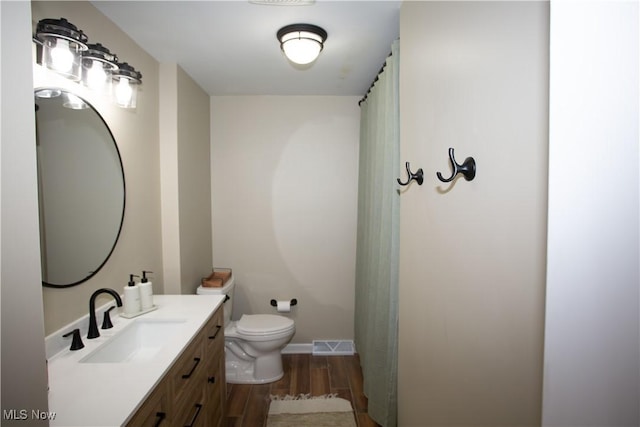 full bath with visible vents, toilet, wood finished floors, baseboards, and vanity