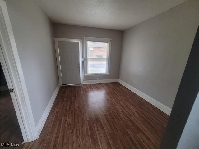 empty room featuring baseboards, a textured ceiling, and dark wood finished floors