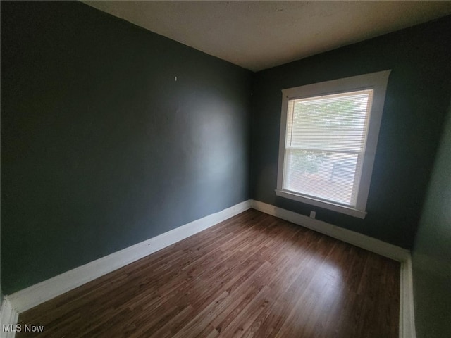 spare room featuring baseboards and dark wood-style flooring