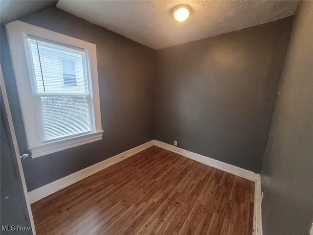 spare room featuring a textured ceiling, baseboards, and dark wood-style flooring