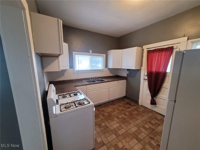 kitchen with a sink, white appliances, dark countertops, and white cabinetry