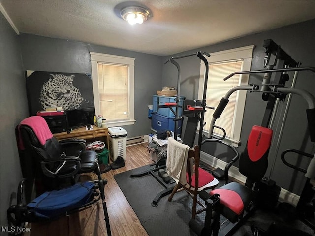 workout area featuring a baseboard radiator, baseboards, and wood finished floors