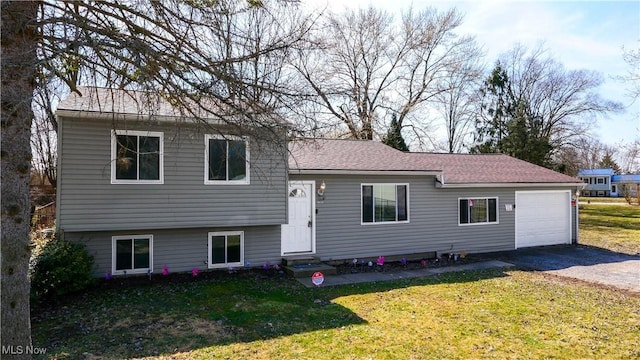 tri-level home with driveway, entry steps, a front yard, a shingled roof, and an attached garage