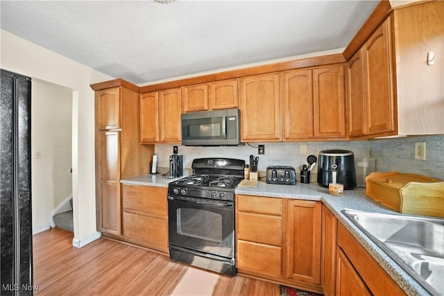 kitchen with tasteful backsplash, light countertops, light wood-type flooring, gas stove, and a sink