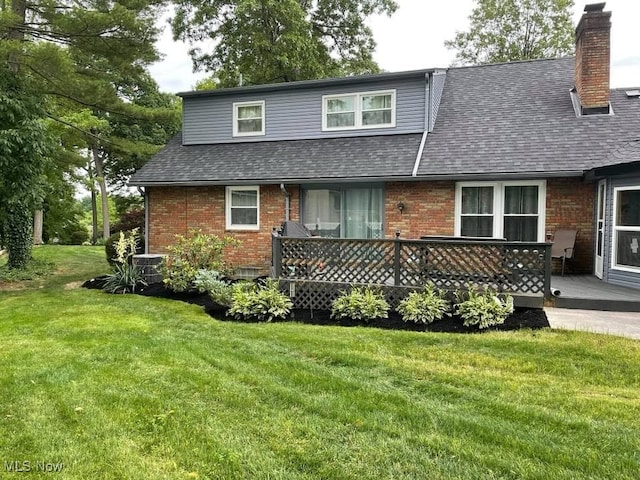 view of front of property featuring roof with shingles, a chimney, a front lawn, a deck, and brick siding