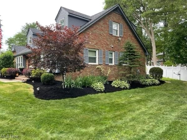 view of side of home featuring a lawn, brick siding, and fence