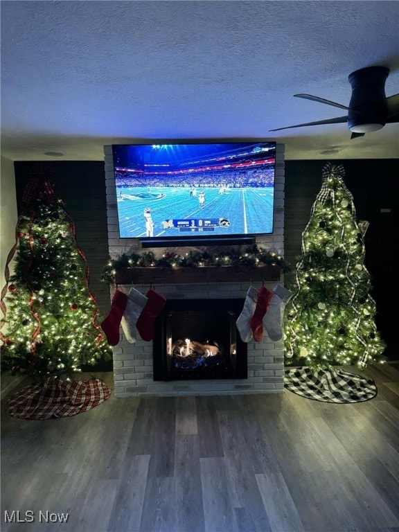 home theater room with a textured ceiling, a brick fireplace, wood finished floors, and a ceiling fan