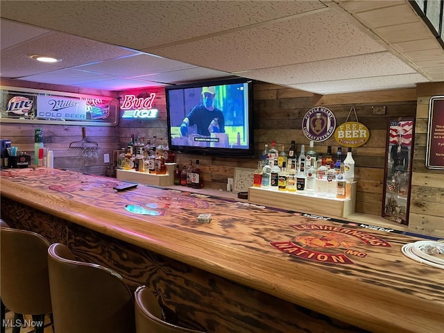 bar featuring a paneled ceiling, wooden walls, and a bar