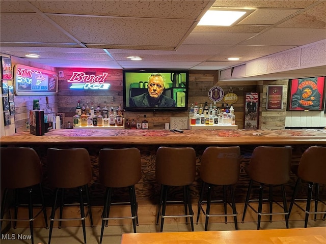 bar featuring a drop ceiling, a bar, and wood walls