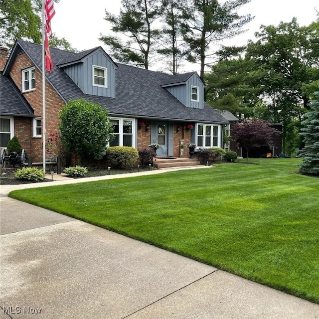 new england style home featuring brick siding, a front lawn, and roof with shingles