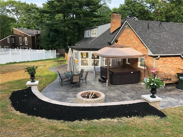 back of property with brick siding, a hot tub, a patio, and fence