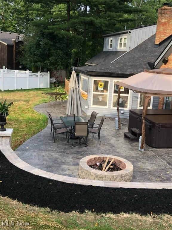 view of patio / terrace featuring fence, a fire pit, outdoor dining space, and a hot tub