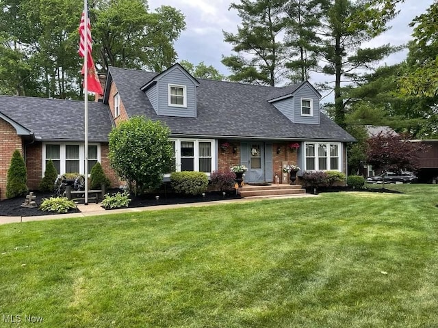 cape cod-style house featuring brick siding, a front yard, and roof with shingles