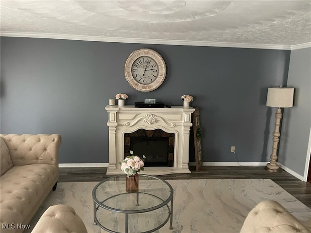 living room with a fireplace with raised hearth, a textured ceiling, crown molding, and baseboards