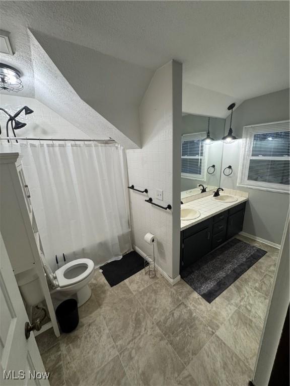 full bath with a sink, lofted ceiling, toilet, and double vanity