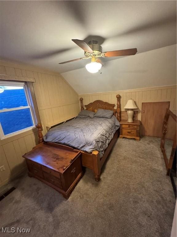 bedroom with vaulted ceiling, wooden walls, carpet flooring, and ceiling fan