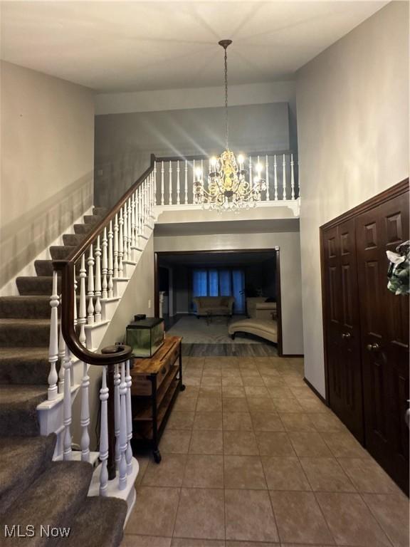 tiled foyer entrance with an inviting chandelier, stairway, and a high ceiling