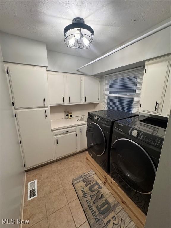 washroom with light tile patterned floors, visible vents, cabinet space, a textured ceiling, and washing machine and dryer