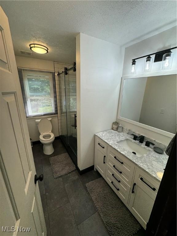 full bath featuring vanity, visible vents, a stall shower, a textured ceiling, and toilet