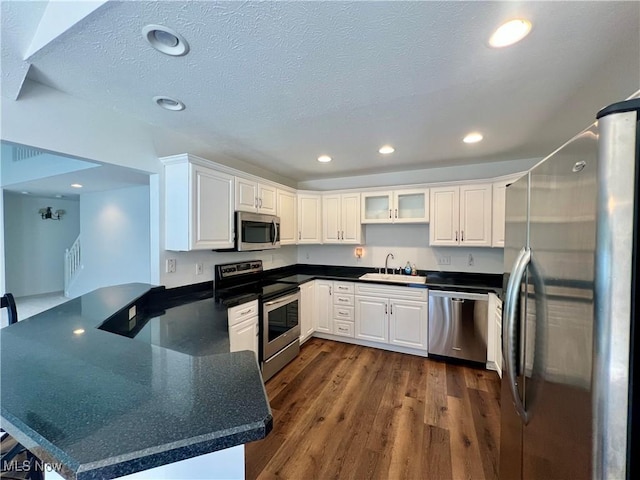 kitchen featuring a sink, a peninsula, dark countertops, and stainless steel appliances