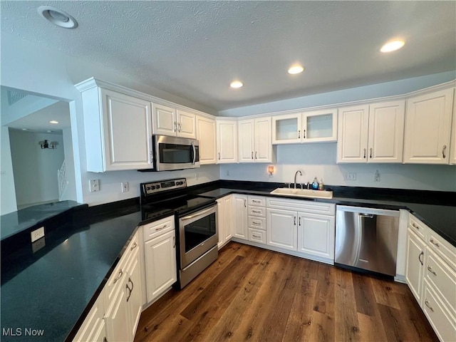 kitchen with dark countertops, a sink, stainless steel appliances, white cabinetry, and dark wood-style flooring