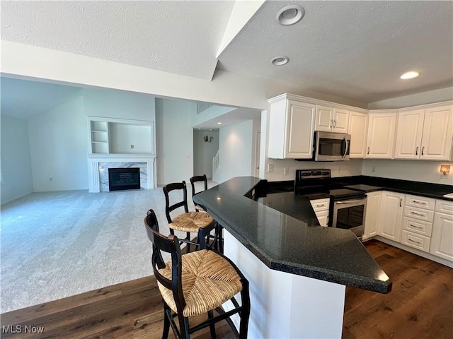 kitchen featuring a breakfast bar, appliances with stainless steel finishes, a fireplace, a peninsula, and white cabinetry