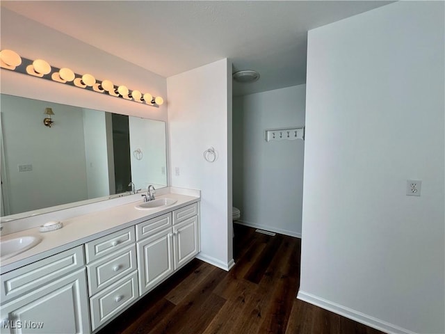 bathroom with baseboards, toilet, double vanity, wood finished floors, and a sink