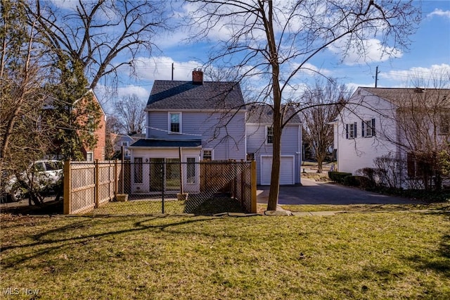 rear view of property featuring fence, roof with shingles, a chimney, a yard, and driveway