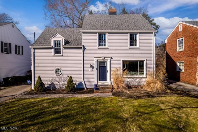 traditional-style home featuring a shingled roof, a front yard, and a chimney