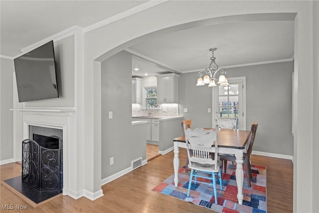 dining area featuring visible vents, arched walkways, light wood-style floors, crown molding, and baseboards